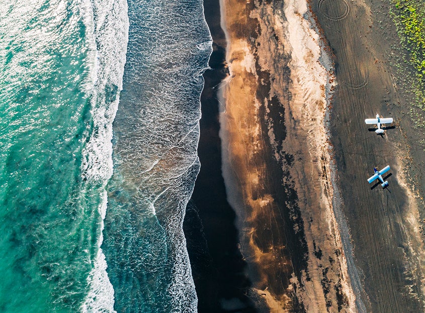 Aerial view of ocean waves meeting a sandy shoreline with small boats